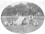 Portrait of young men relaxing outside tent. One plays an accordion.