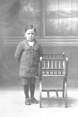Portrait of solemn young boy standing by chair