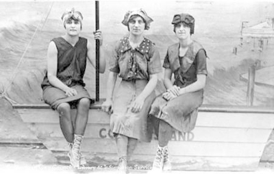 Studio portrait of three young ladies sitting on the edge of a boat wearing swimming costumes