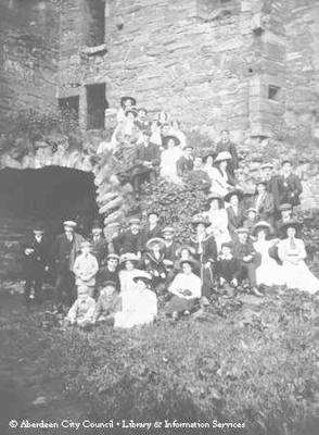 Picnic scene of ladies and young men in the grounds of a ruined castle