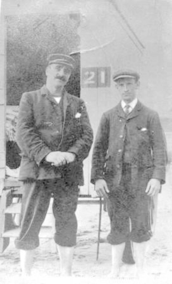Portrait of two gentlemen at the sea side standing in front of a bathing machine.